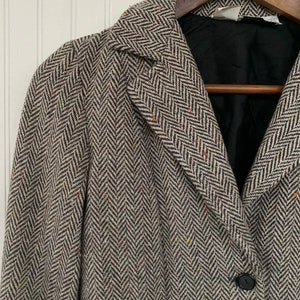 Op de afbeelding: Een bruin en wit herringbone tweed blazer met een enkele knoopsluiting. De blazer heeft een zwarte voering en een kraag.