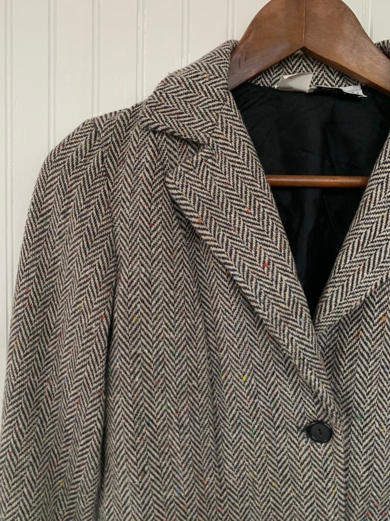 Op de afbeelding: Een bruin en wit herringbone tweed blazer met een enkele knoopsluiting. De blazer heeft een zwarte voering en een kraag.