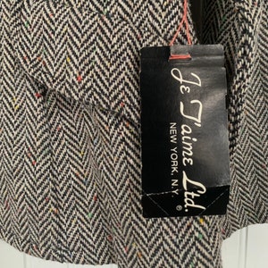 Op de afbeelding: Een zwart-witte herringbone tweed stof met een zwart label waarop "Je T'aime Ltd. New York, N.Y." staat.
