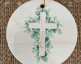 May include: White ceramic ornament with a gold cross surrounded by green leaves. The word "faith" is written in gold script on the ornament.