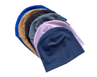 Op de afbeelding: Een stapel van zes beanies in verschillende kleuren, waaronder blauw, bruin, zwart, grijs, roze en denim.