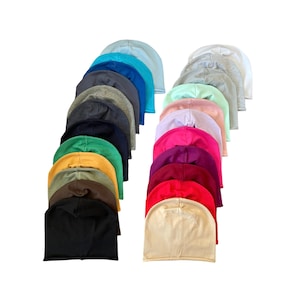 Puede incluir: Una colección de 18 gorros de lana en varios colores, incluyendo negro, blanco, gris, rojo, rosa, azul, verde y amarillo. Los gorros están dispuestos en una fila, con los colores alternando.