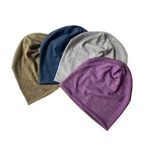 Może przedstawiać: Cztery czapki beanie w różnych kolorach: oliwkowo-zielonym, granatowym, szarym i fioletowym. Czapki są wykonane z miękkiej, elastycznej tkaniny.