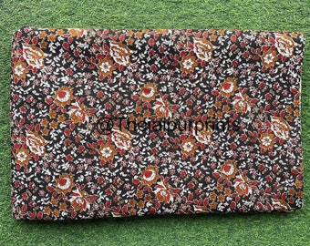 May include: A black fabric with a floral print in shades of brown, red, and white. The fabric is folded in half and laid flat on a green surface.