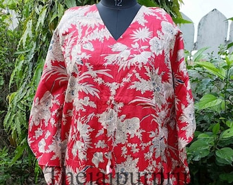 Peut inclure: Un caftan rouge avec un motif floral beige et gris. Le caftan a un col en V et des manches larges. Le texte "The Jaipur" est imprimé sur le devant.