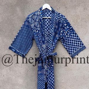 Op de afbeelding: Een blauw-witte badjas met bijpassende riem hangt aan een witte hanger. De badjas heeft verschillende geometrische en bloemmotieven in blauwtinten. De tekst "@thejaipurprints" is onderaan zichtbaar.