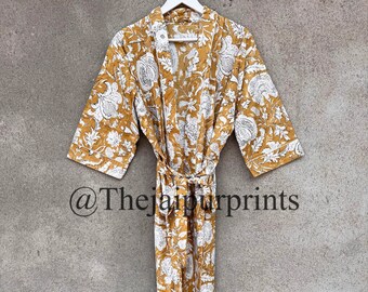 May include: A mustard yellow cotton robe with a white floral print. The robe has a tie belt and long sleeves. The robe is hanging on a hanger against a gray wall. The text "@Thejaipurprints" is visible in the bottom left corner of the image.