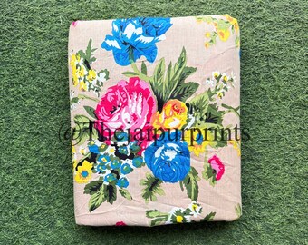 May include: A beige fabric with a floral print featuring pink, yellow, blue, and green flowers. The fabric has a subtle texture and a soft, natural feel.