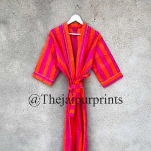 May include: A pink and orange striped robe with a white trim and a tie belt. The robe is hanging on a white hanger against a gray wall. The text "@Thejaipurprints" is visible at the bottom of the image.