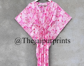 Peut inclure: Une robe caftan à imprimé floral rose suspendue à un cintre blanc. La robe a un col en V et une taille à cordon. Le tissu est rose clair avec un motif floral rose plus foncé. Le texte "@Thejaipurprints" est visible.