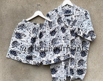 Puede incluir: Un conjunto de pijama blanco y azul estampado con una parte superior de manga corta y pantalones cortos. La parte superior tiene cuello y cierre de botones. Los pantalones cortos tienen una cintura elástica.