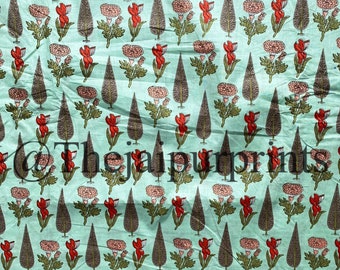 Op de afbeelding: Een teal stof met een herhalend patroon van rode en roze bloemen, groene bladeren en bruine boomsilhouetten.