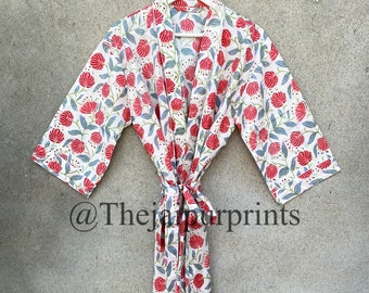 Op de afbeelding: Een witte bloemenbadjas met een patroon van rode en blauwe bloemen. De badjas is in de taille geknoopt en hangt aan een witte hanger. De tekst "@thejaipurprints" is linksonder zichtbaar.