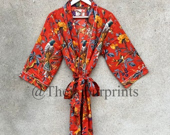 Op de afbeelding: Rode badjas met bloemenprint met een vogel- en bloemenpatroon. De badjas heeft een witte bies en een bijpassende riem. Hij hangt aan een witte hanger tegen een grijze achtergrond.