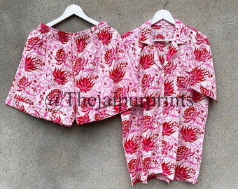 Puede incluir: Un conjunto de pijama a juego con una camisa de manga corta con botones y pantalones cortos. El conjunto es blanco con un patrón repetido de diseños florales rosas y rojos. Los artículos están colgados en perchas blancas sobre un fondo gris. El texto "@Thejaipurprints" es visible.