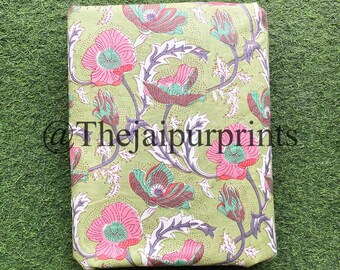 Op de afbeelding: Groene stof met een bloemenprint met roze, groene en bruine bloemen. De stof heeft een witte achtergrond met kleine witte stippen.