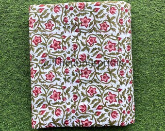 May include: White cotton fabric with a floral print in shades of pink, green, and brown. The fabric is folded in half and laid on a green surface.