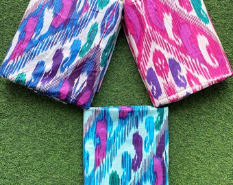 Könnte beinhalten: Drei Stoffquadrate mit einem bunten Ikat-Muster. Die Quadrate sind gefaltet und in Dreiecksform auf einer grünen Oberfläche angeordnet.