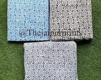 May include: Three fabric swatches with a white and blue geometric pattern. The swatches are folded and laid out on a green surface.