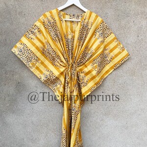 May include: Yellow and black striped kaftan dress with a tiger print design. The dress has a V-neck and a drawstring waist. The text "@Thejaipurprints" is visible in the lower left corner. The dress is hanging on a white hanger.