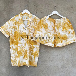 May include: A white and yellow pajama set with a tropical print featuring palm trees and birds. The set includes a short-sleeved shirt with a button-down collar and matching shorts. The text "@Thejaipurprints" is visible on the shirt.