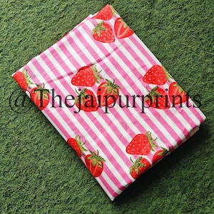 May include: A folded fabric with a pink and white striped pattern, adorned with illustrations of red strawberries. The fabric has the text "@thejaipurprints" printed on it.