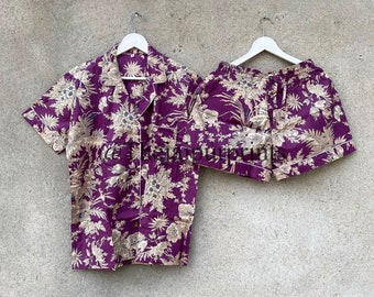 Puede incluir: Un conjunto de pijama de estampado floral morado y dorado con una camisa de manga corta abotonada y pantalones cortos a juego.