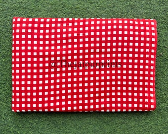 May include: A folded red fabric with a white square grid pattern. The fabric is rectangular and lies on a green surface. The text "@Thejaipurprints" is visible on the fabric.