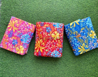 May include: Three fabric swatches with a floral pattern. The swatches are folded and arranged in a row on a green surface. The swatches are pink, red, and blue.