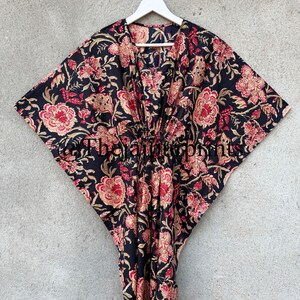 May include: A black kaftan with a floral print in shades of red, gold, and cream. The kaftan has a V-neckline and a tie at the waist.