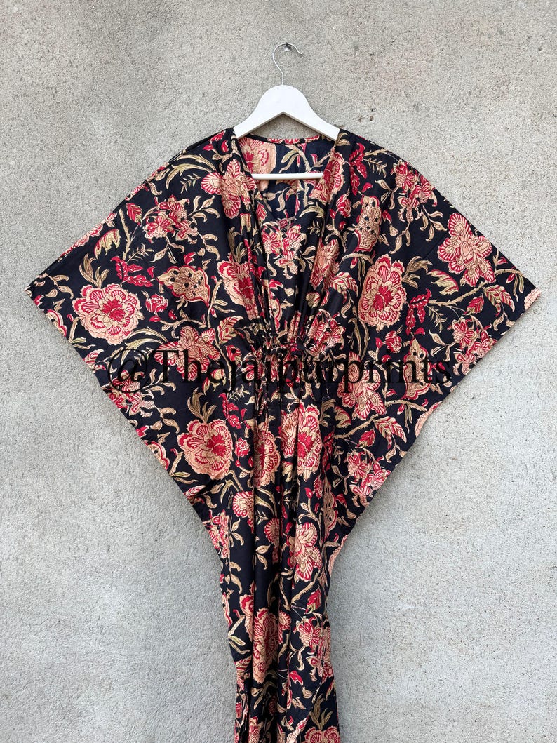 May include: A black kaftan with a floral print in shades of red, gold, and cream. The kaftan has a V-neckline and a tie at the waist.