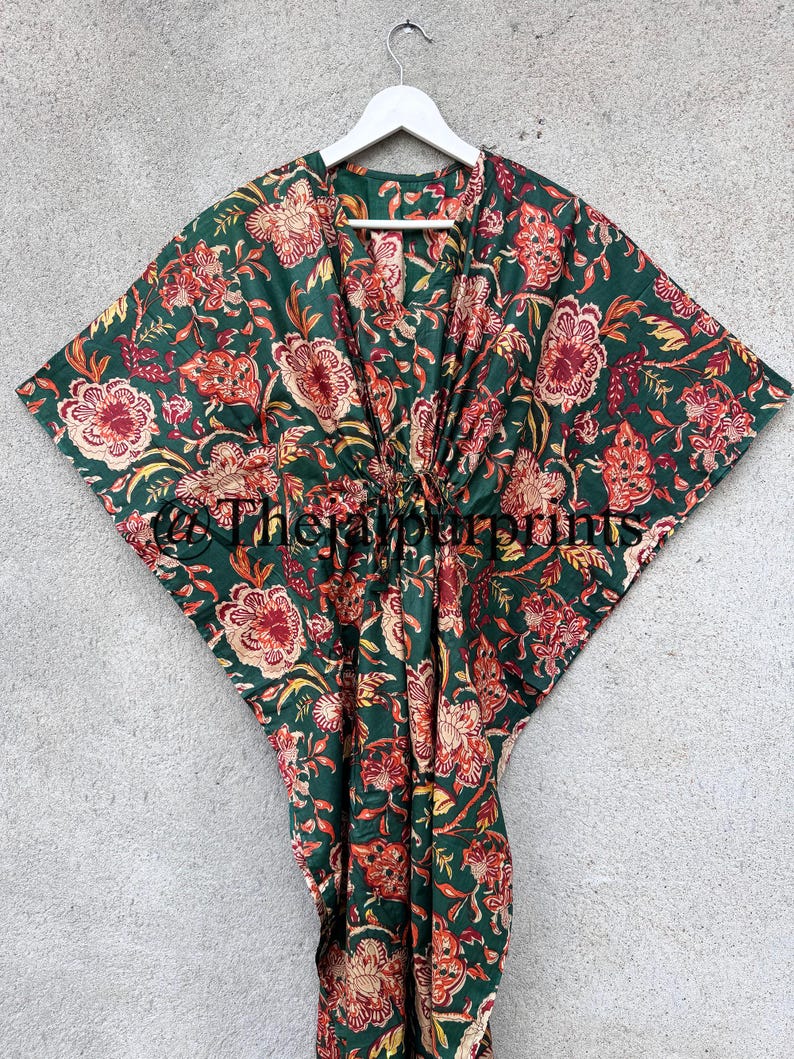 May include: A green cotton kaftan with a floral print in shades of red, orange, and yellow. The kaftan has a V-neck and a tie at the waist.