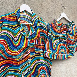 May include: A colorful pajama set with a wavy, abstract print in shades of blue, red, yellow, green, and white. The set includes a short-sleeved shirt with a button-up closure and matching shorts.
