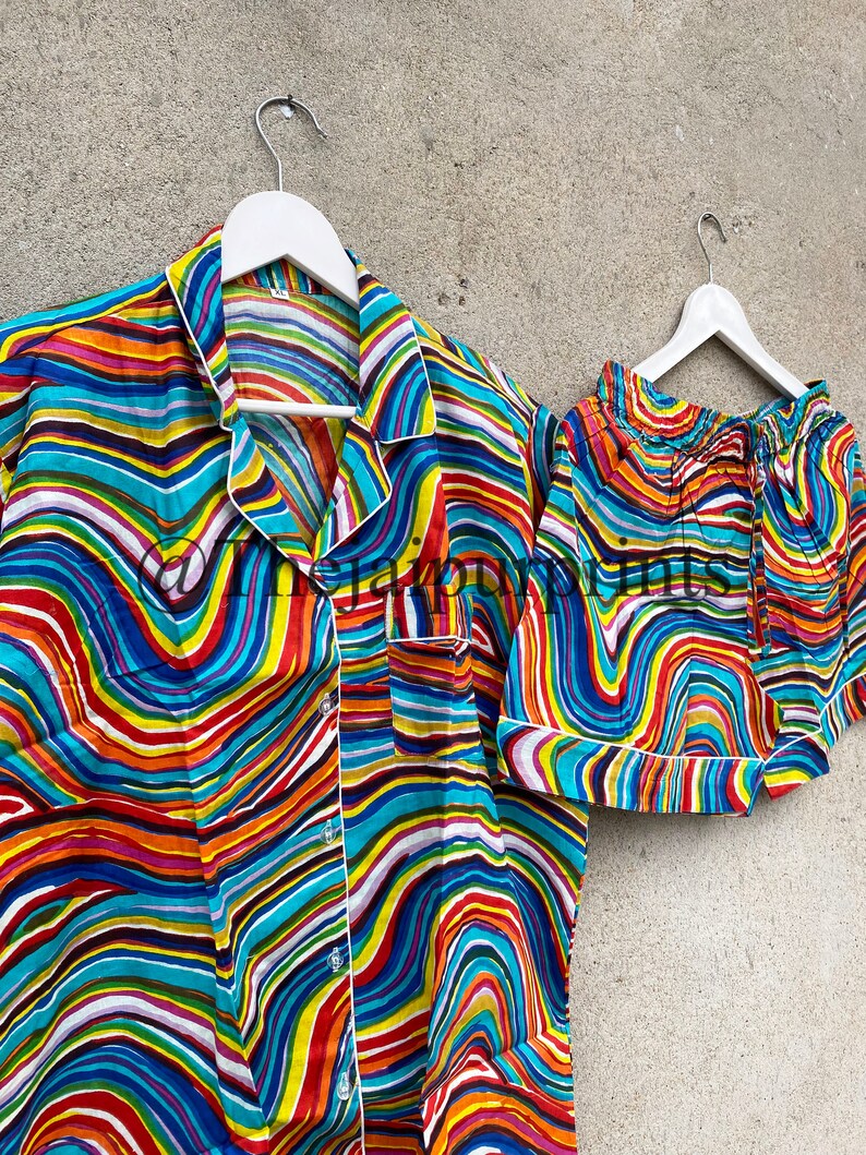 May include: A colorful pajama set with a wavy, abstract print in shades of blue, red, yellow, green, and white. The set includes a short-sleeved shirt with a button-up closure and matching shorts.