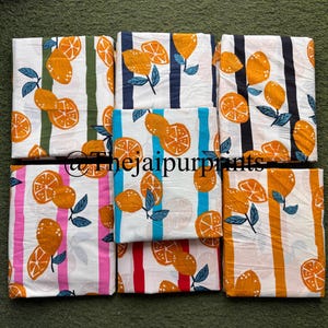 May include: Folded fabric pieces with a white base, featuring a pattern of oranges and green leaves. The fabric is striped vertically in green, blue, pink, and orange. The image includes the text "@thejaipurprints".