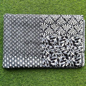 以下が含まれることがあります： 黒と白の綿生地で、パッチワークのデザインが施されています。幾何学模様と花柄が組み合わされています。