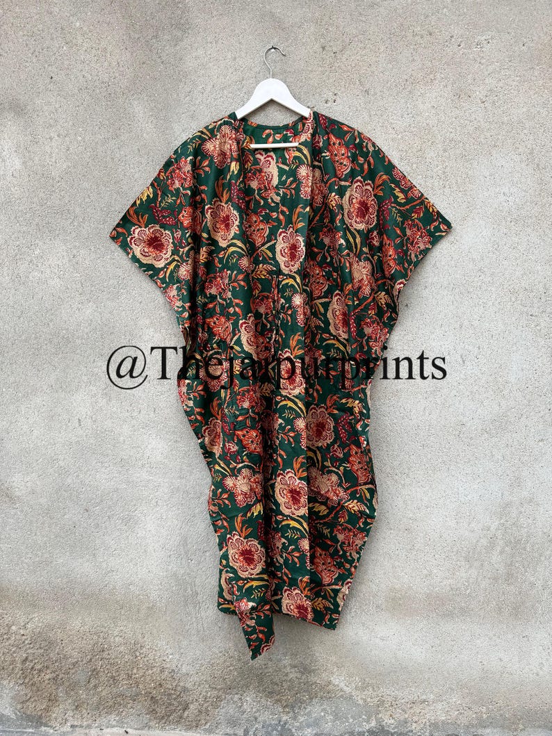 May include: A green kimono with a floral print in shades of orange and white. The kimono is hanging on a white hanger against a gray wall. The text "@TheSimplePrints" is visible in the lower left corner of the image.