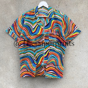 May include: A short-sleeved button-up shirt with a colorful abstract wavy pattern in shades of red, orange, yellow, green, blue, and purple. The shirt has a white collar and a white button placket.