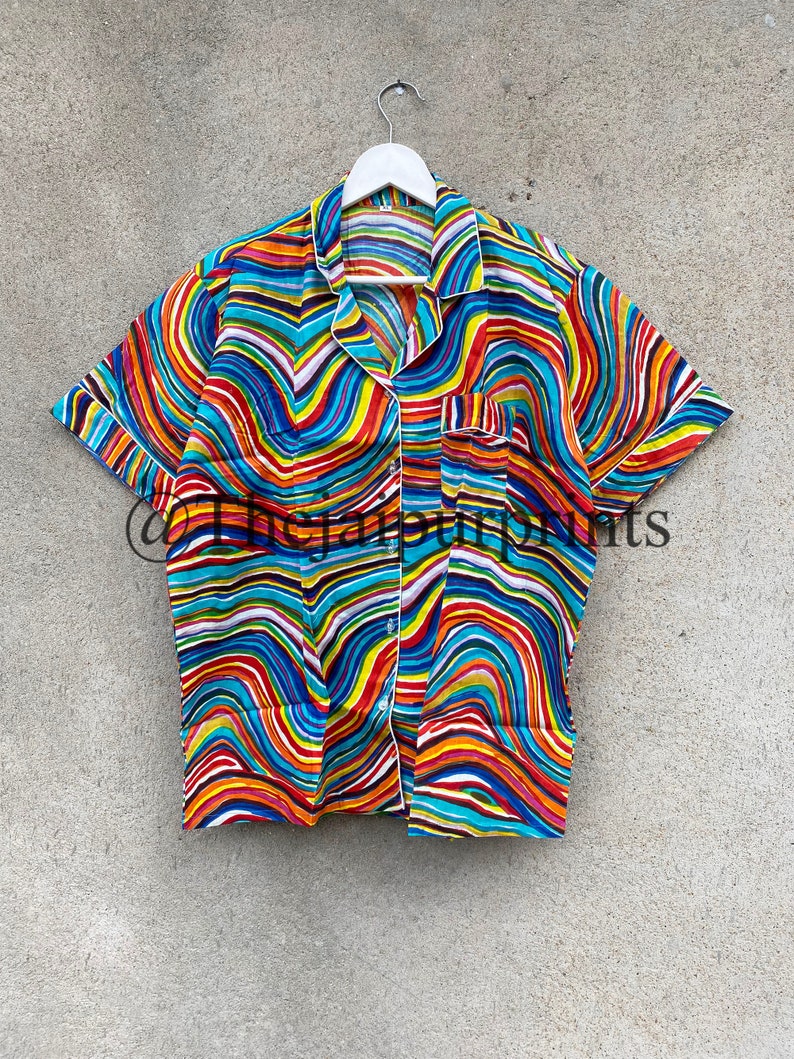 May include: A short-sleeved button-up shirt with a colorful abstract wavy pattern in shades of red, orange, yellow, green, blue, and purple. The shirt has a white collar and a white button placket.