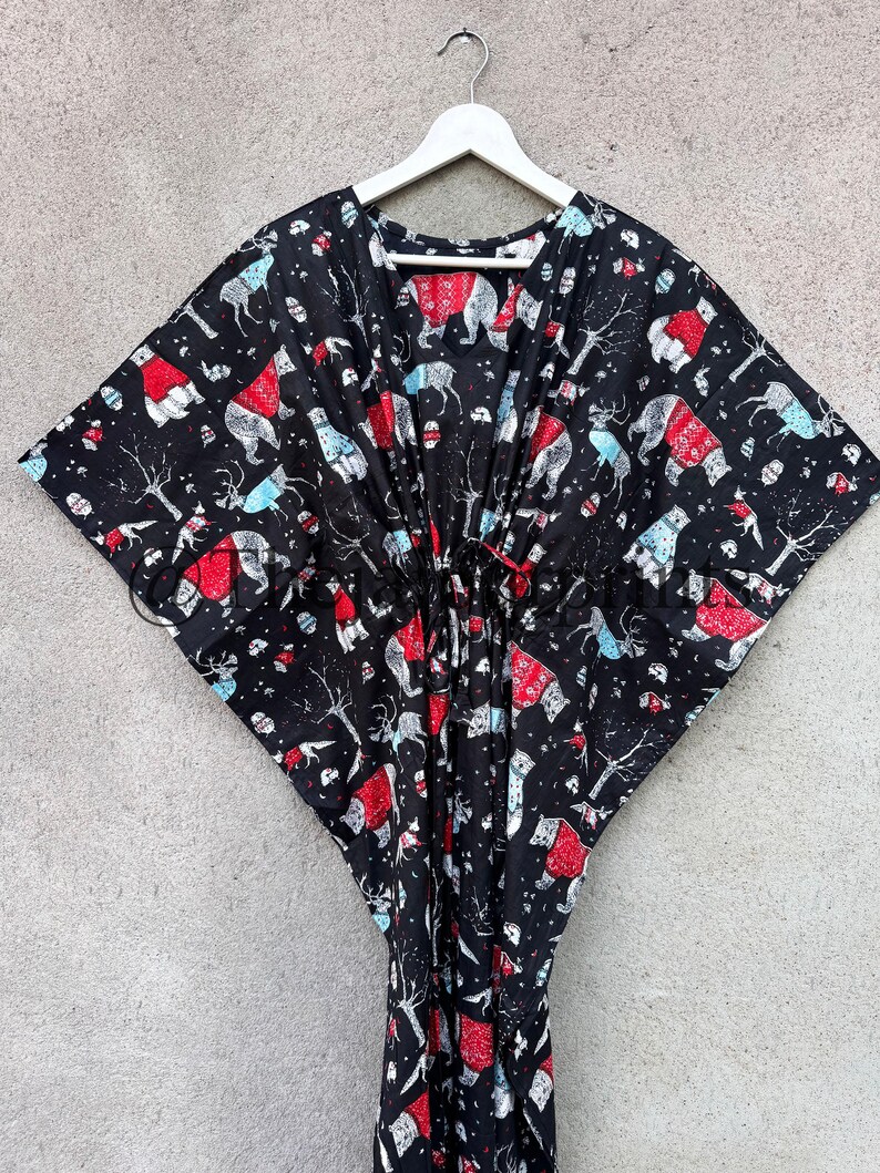May include: Black kaftan with a white hanger. The kaftan has a red and white print of polar bears wearing red hats and scarves. The print also includes trees, birds, and other wintery elements.