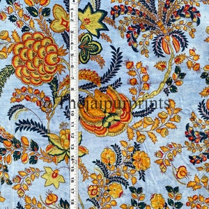 May include: A light blue fabric with a floral pattern in shades of yellow, orange, and green. The fabric has a repeating pattern of flowers and leaves.