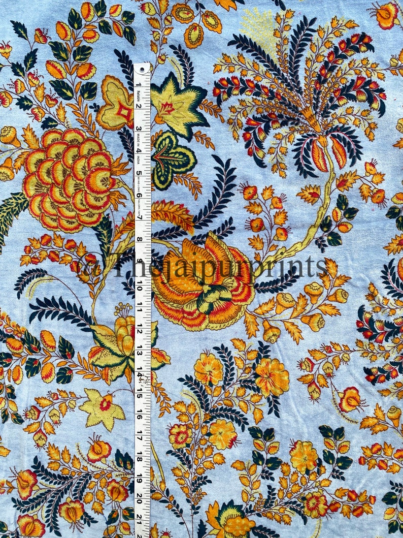 May include: A light blue fabric with a floral pattern in shades of yellow, orange, and green. The fabric has a repeating pattern of flowers and leaves.
