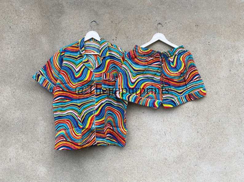May include: A colorful pajama set with a short-sleeved button-up shirt and matching shorts. The fabric features a wavy, abstract pattern in shades of blue, red, yellow, and white.