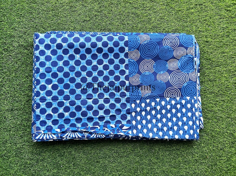 May include: A blue and white fabric with a patchwork design. The fabric features three different patterns: polka dots, concentric circles, and a repeating teardrop shape.