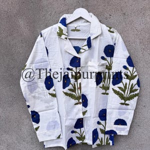May include: White pajama top with a blue floral pattern. The long-sleeved shirt has a collared neckline and a pocket on the chest. The floral design features blue flowers and green leaves. The shirt is hanging on a white hanger.
