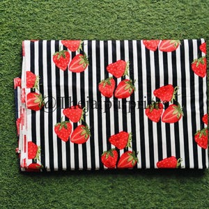 May include: Folded fabric with a black and white striped pattern. The fabric is decorated with red strawberries with green leaves. The text "@thejaprints" is visible on the fabric.
