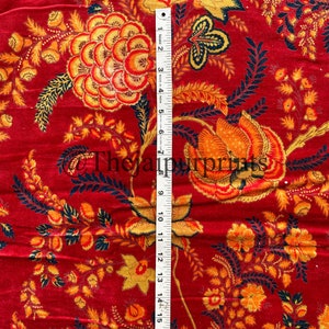 May include: Red fabric with a floral pattern in shades of orange, yellow, and black. The fabric is measured with a ruler that shows 18 inches.