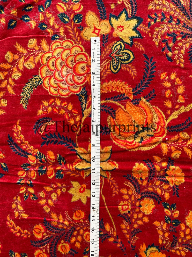May include: Red fabric with a floral pattern in shades of orange, yellow, and black. The fabric is measured with a ruler that shows 18 inches.