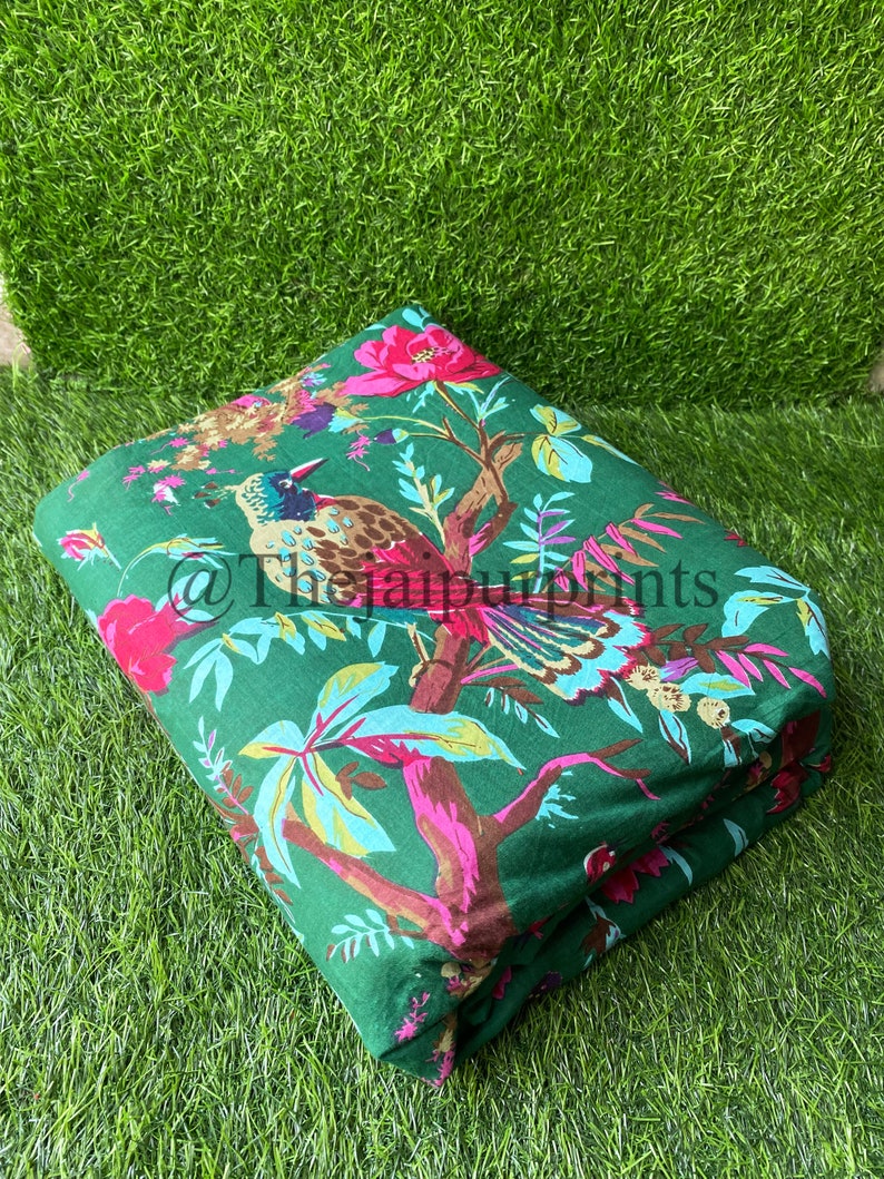 Op de afbeelding: Groene stof met een bloemen- en vogelprint. De stof heeft roze bloemen, groene bladeren en een bruine en blauwe vogel.