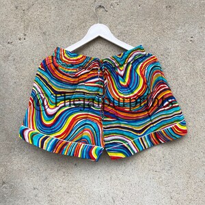 May include: Colorful patterned shorts with a white elastic waistband and a white trim around the edges. The shorts have a wavy, abstract design in shades of blue, red, yellow, orange, and green.